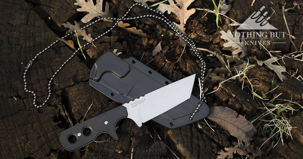 An overhead shot of the Cold Steel 49HTF Mini Tac Tanto Neck Knife on top of its sheath surrounded by oak leaves