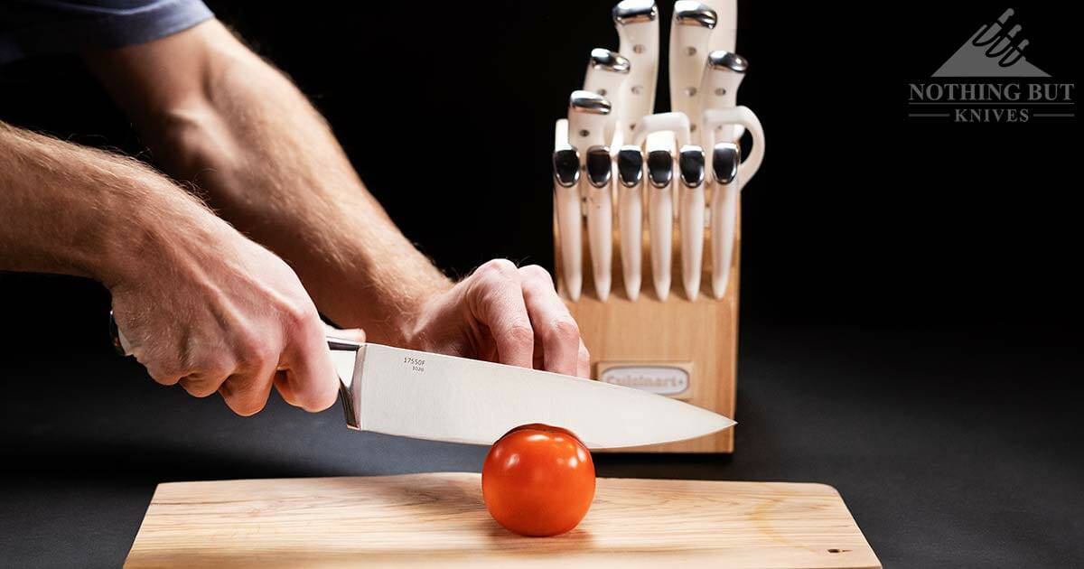 The Cuisinart-C77WTR chef knife slicing through a tomato in the foreground with the rest of the kitchen knife set in the background. 
