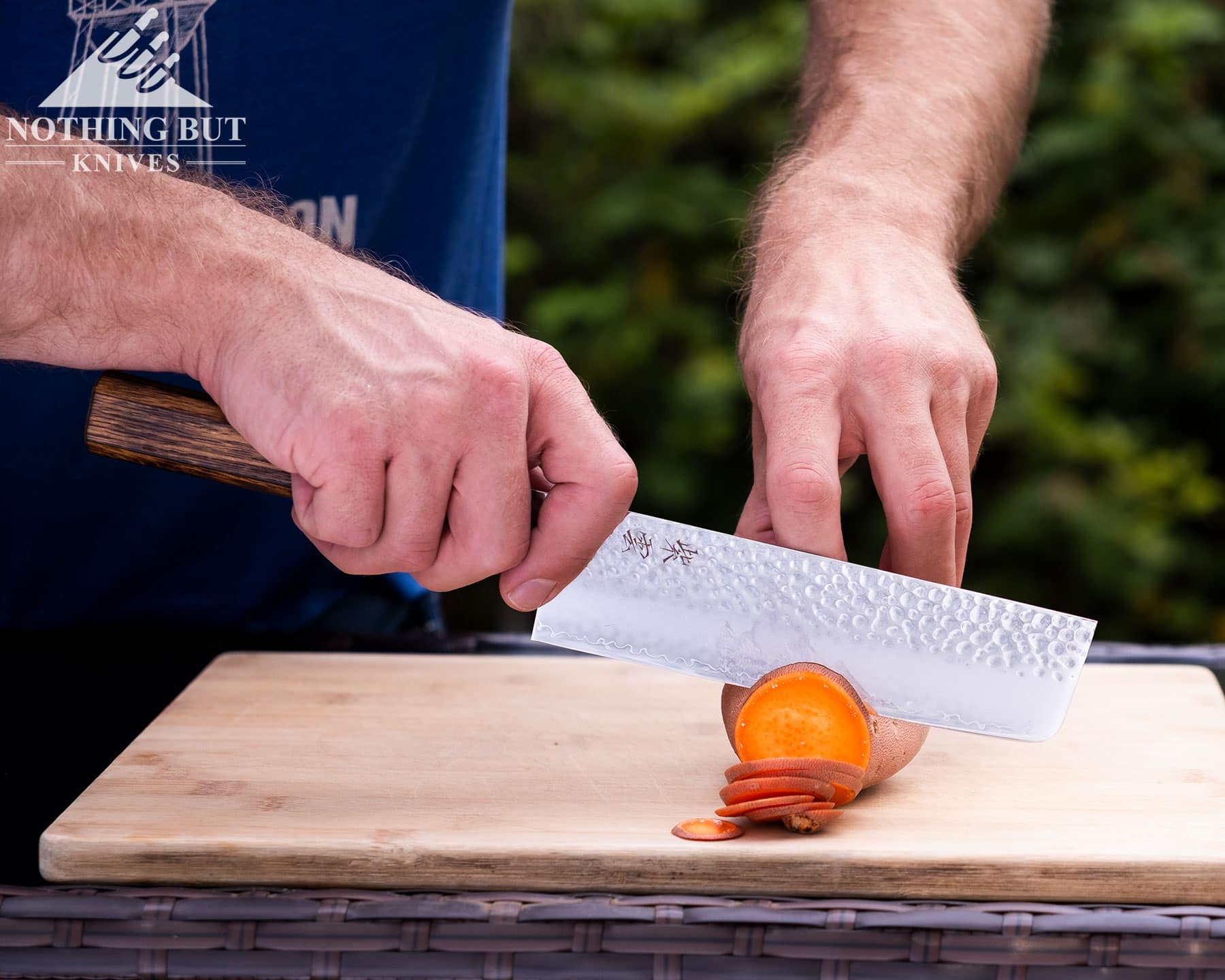 Our Ongoing Hunt For Great Japanese Knife Sets - Image 29 A close-up of the Demko Nakiri style cleaver being used to slice a sweet potato on a bamboo cutting board.