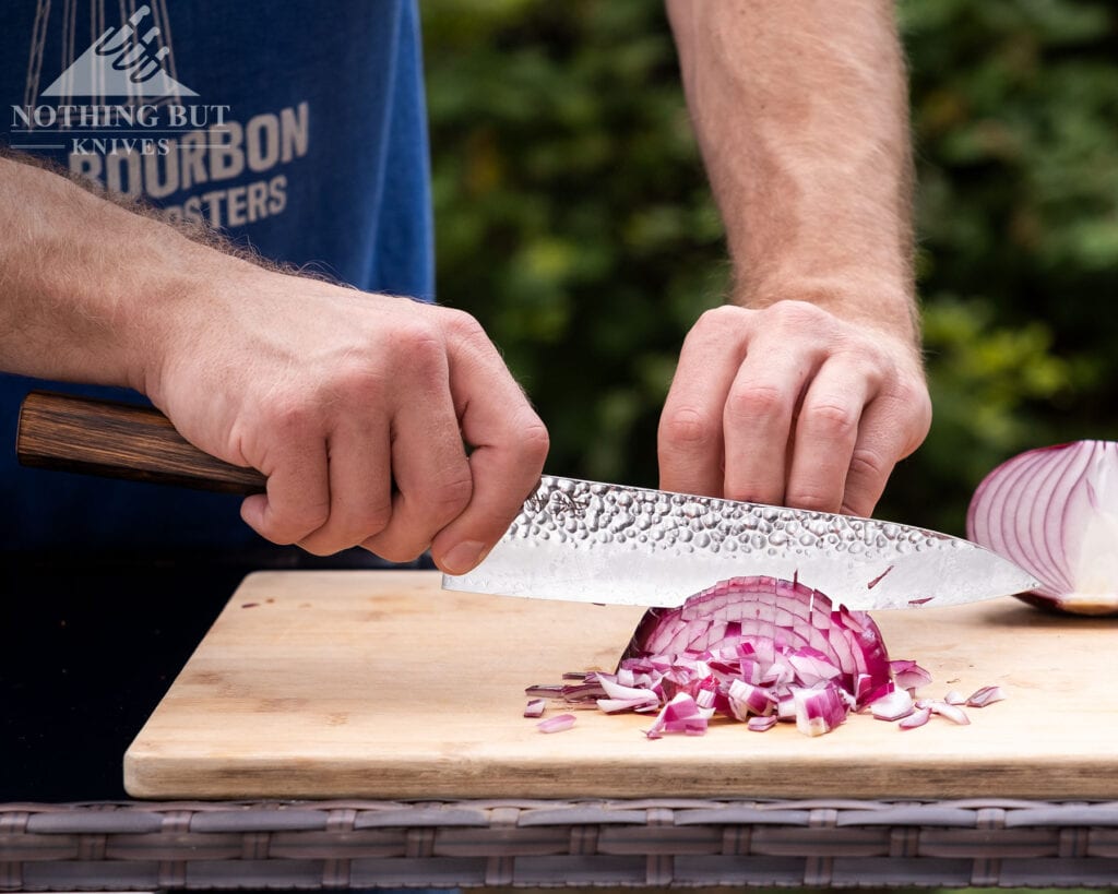 Our Ongoing Hunt For Great Japanese Knife Sets - Image 30 A red onion being diced by the Denko Gyuto chef knife outdoors on a wicker counter top in front of a blurry green background.