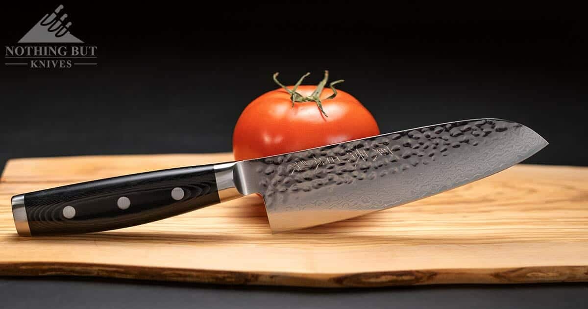 The hammered Damascus steel Enso HD chef knife sitting next to a tomato on a wooden cutting board over a black background. 