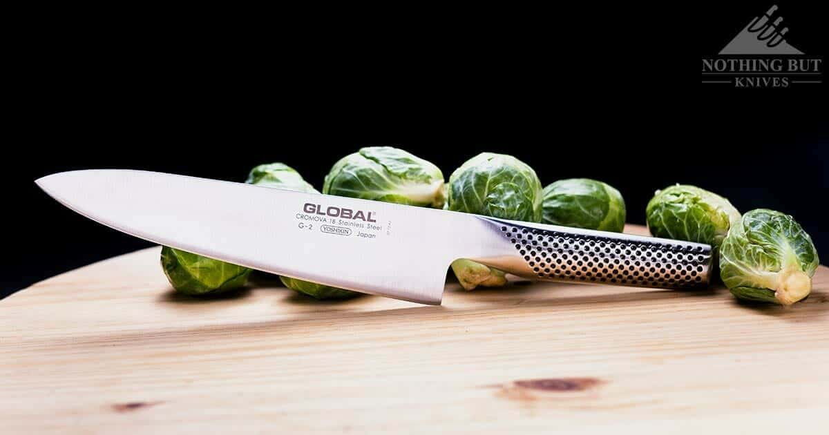 A Global 8 inch chef knife on a wooden cutting board surrounded by Brussel sprouts.