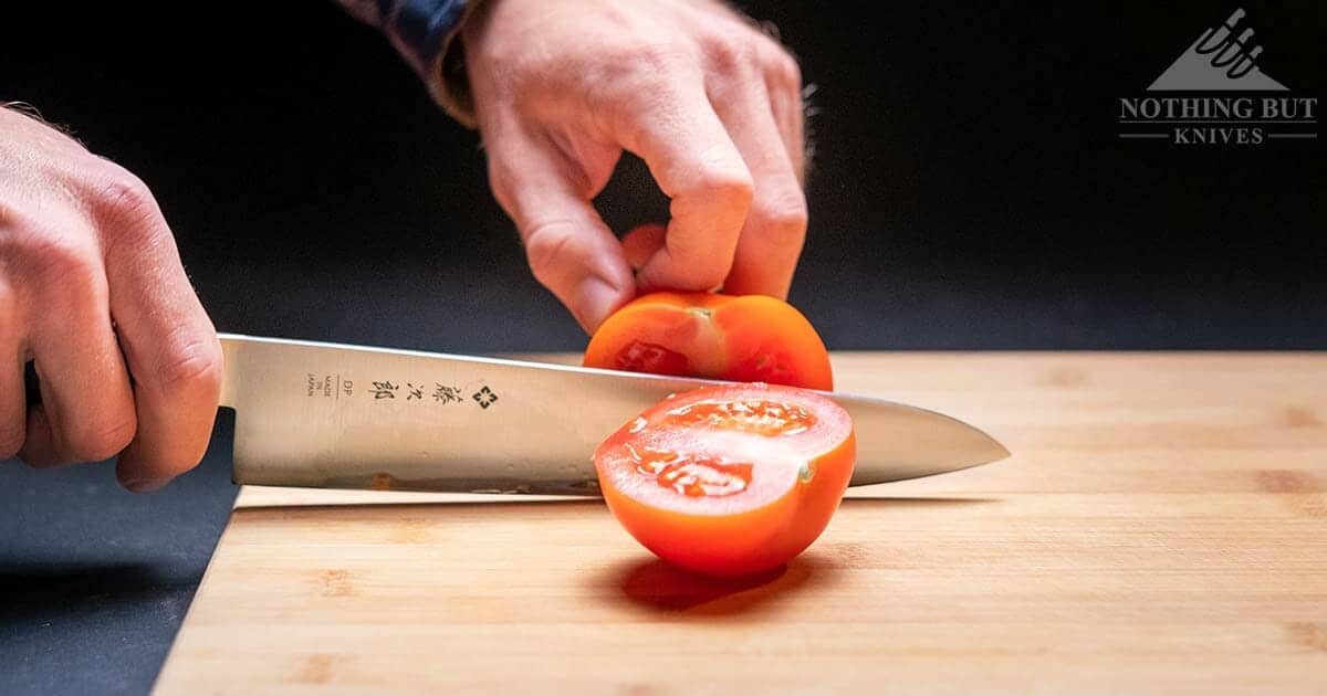 The Tojiro DP F808 chef knife slicing a tomato on a wooden cutting board.