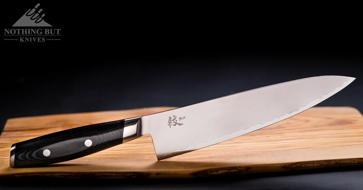 The Yaxell Mon 8 inch Japanese chef knife on a cutting board over a black background. 