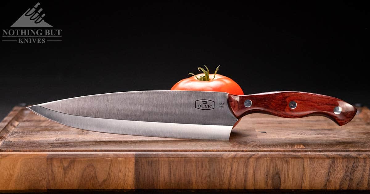 Best Professional And High End Kitchen Knife Sets In 2023 32 Buck 8 inch chef knife next to a tomato on an end grain cutting board.