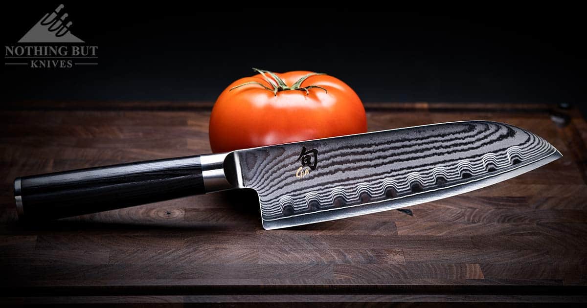 The Shun Classic 7 inch santoku knife next to a tomato on an end grain cutting board. 
