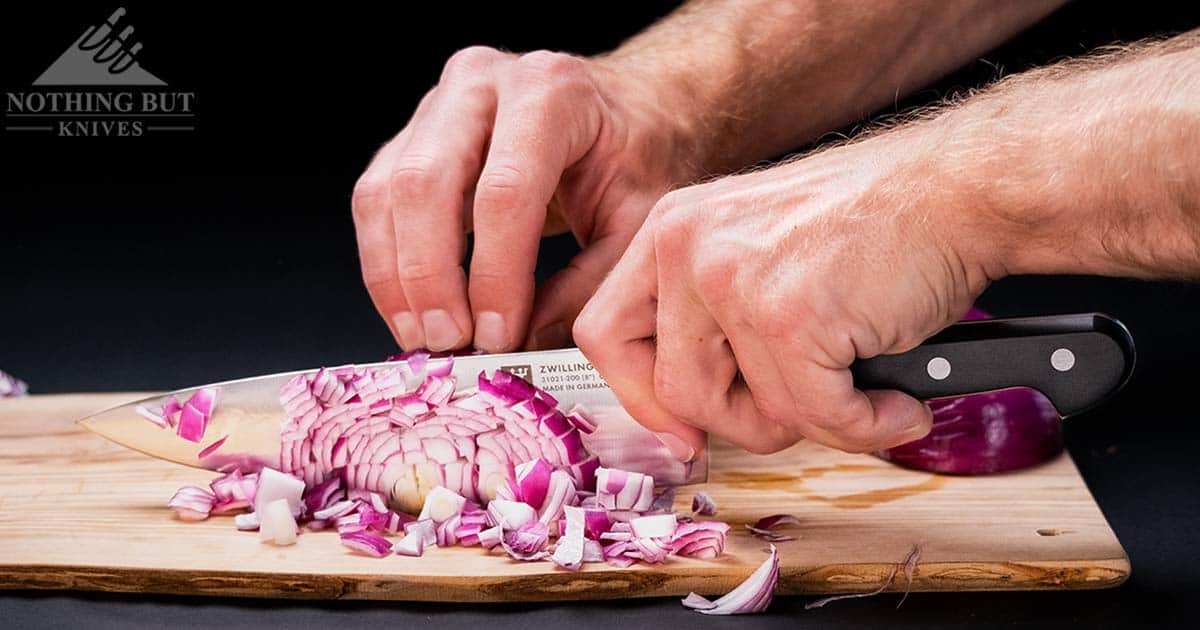 A close up of the Zwilling Processional chef knife chopping onions on a wood cutting board. 