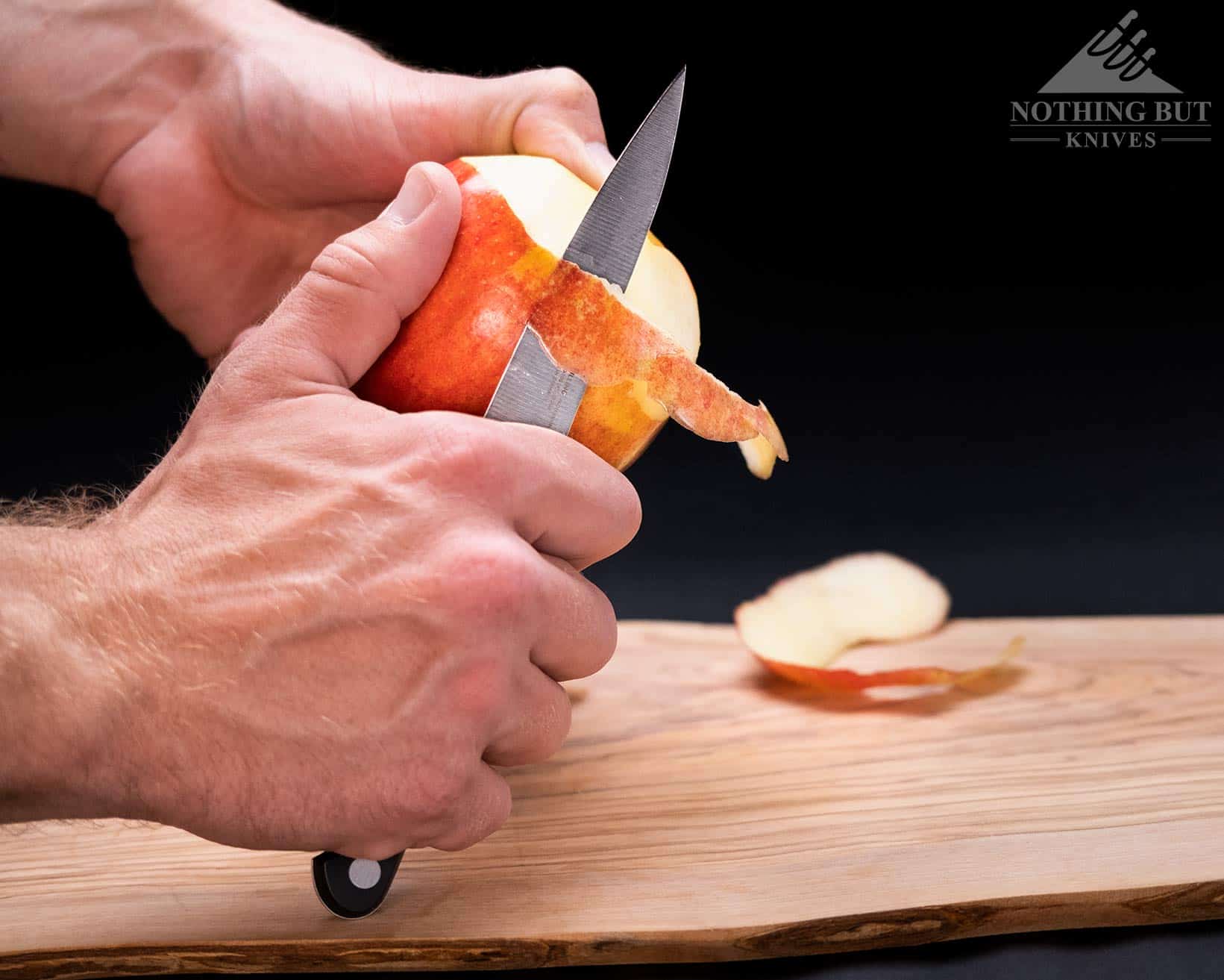 The Zwilling Professional S 4 inch paring knife peeling an apple in front of a dark background.