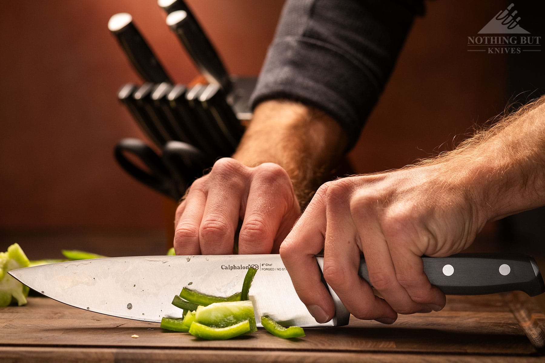 Best Kitchen Knife Sets Under $300 - Image 16 A green Bell pepper being sliced with the Calphalon Precision 8-inch chef knife on a wood cutting board.