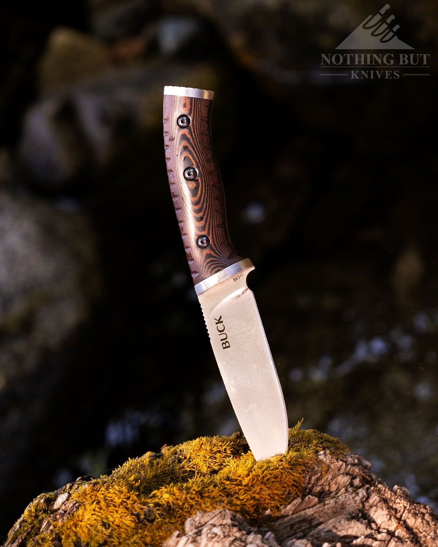 Buck Selkirk Knife Review - Image 1 A close-up of the Buck Selkirk bushcraft knife sticking out of a moss-covered log above a mountain creek.