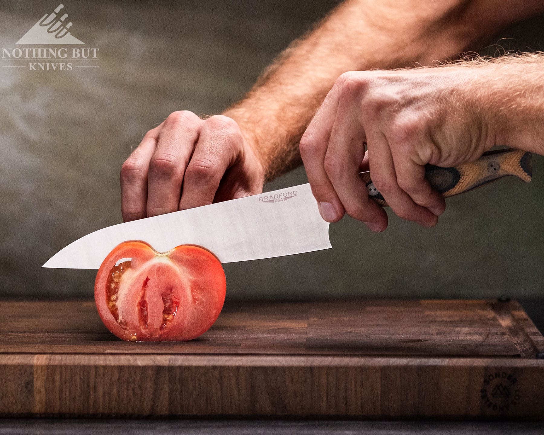 The Ultimate Guide To American Made Knives &Amp; Knife Companies - Image 19 A close-up of a tomato being sliced with the Bradford 8-inch chef knife on a wood cutting board.