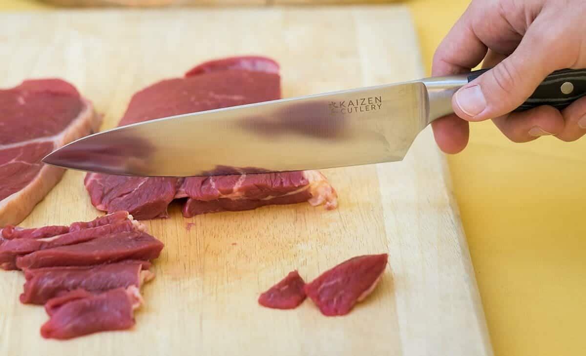 The Kaizen chef knife cutting thin slices of beef.