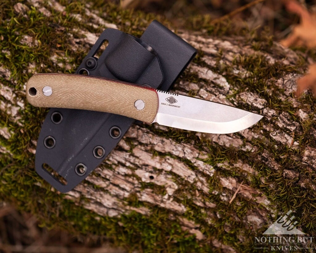 The Ultimate Guide To American Made Knives &Amp; Knife Companies - Image 56 An overhead view of the Knafs Lulu compact bushcraft knife with its kydex sheath on top of a moss-covered log.