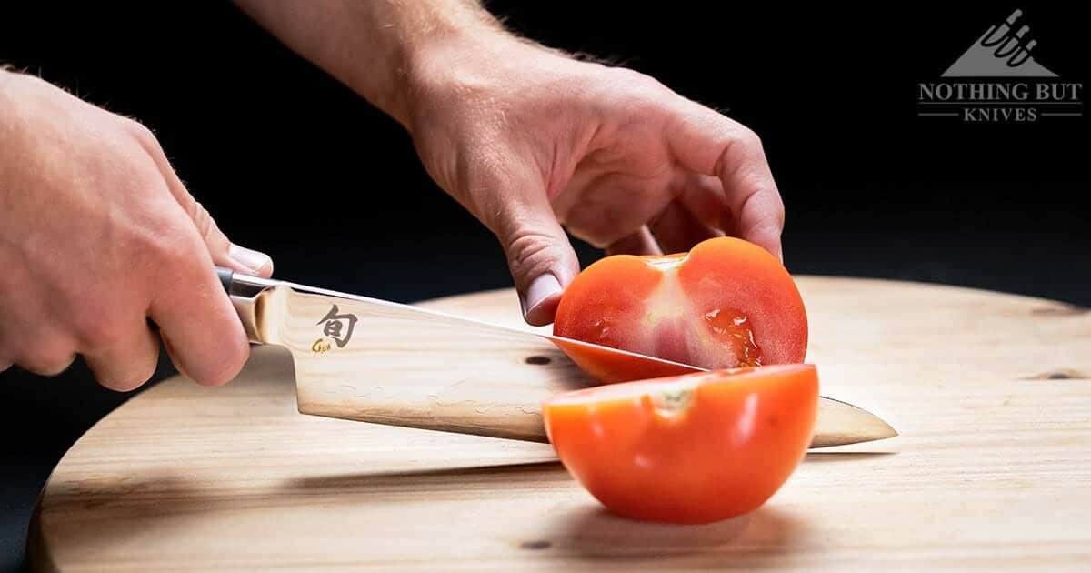 The Shun Sora 8 Inch Chef Knife slicing a tomato in half on a wood cutting board. 