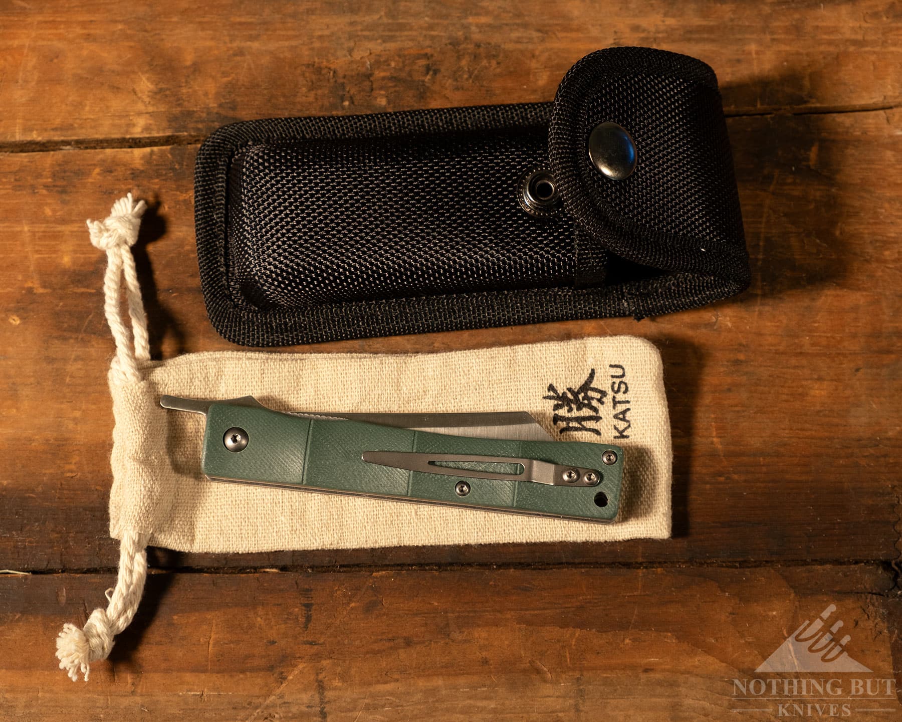 A Few Of Our Favorite Japanese Pocket Knives - Image 6 An overhead image of the Katsu Bamboo pocket knife on a wood table with its pouch and sheath.