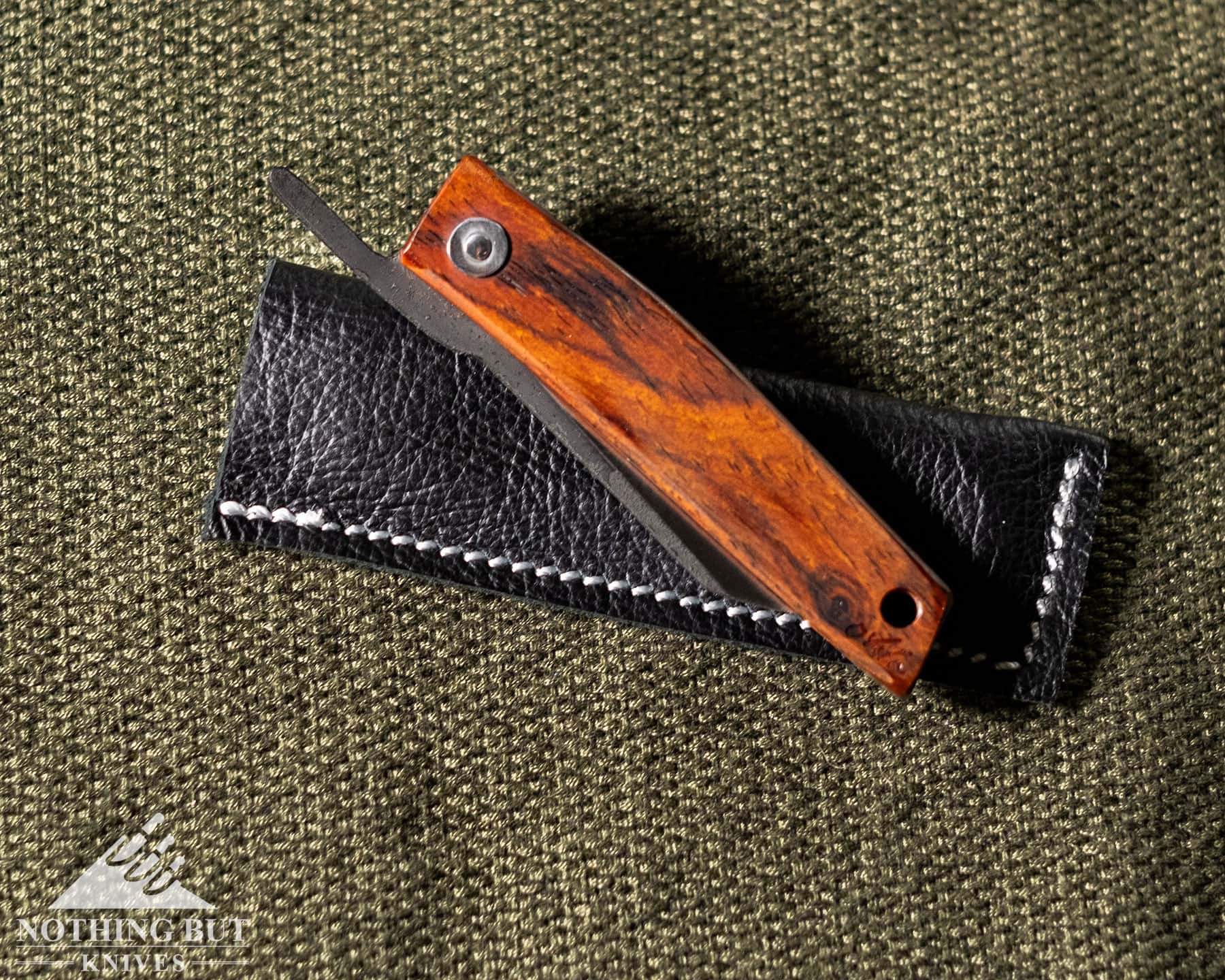 A Few Of Our Favorite Japanese Pocket Knives - Image 3 An overhead view of the Ohta FK5 folding knife in the closed position on top of its black, leather pocket sheath