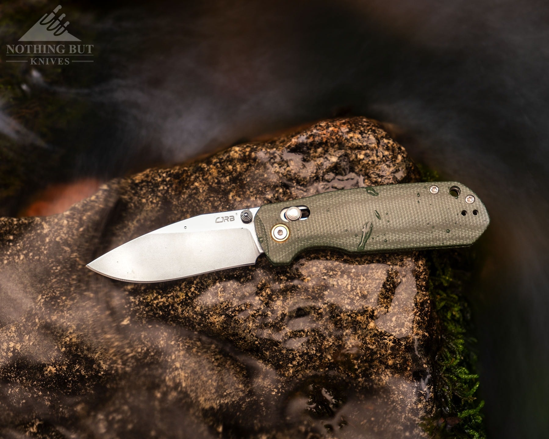 A Few Of Our Favorite Knives With Micarta Handles - Image 12 An overhead angle of the CJRB Maximal folding knife with its blade in the open position on a wet rock next to a mountain creek.