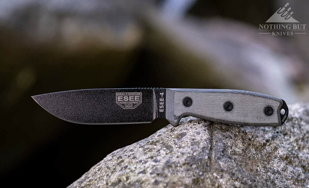 The Esse 4 survival knife with micarta handles sitting on a rock next to a mountain creek. 