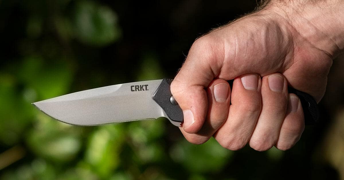 The CRKT pocketknife being gripped in a man's hand in the forest. 