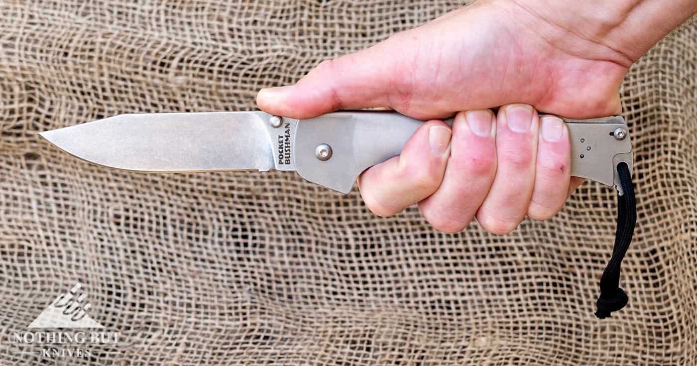 The Cold Steel Pocket Bushman folding knife in a man's hand over a burlap background.