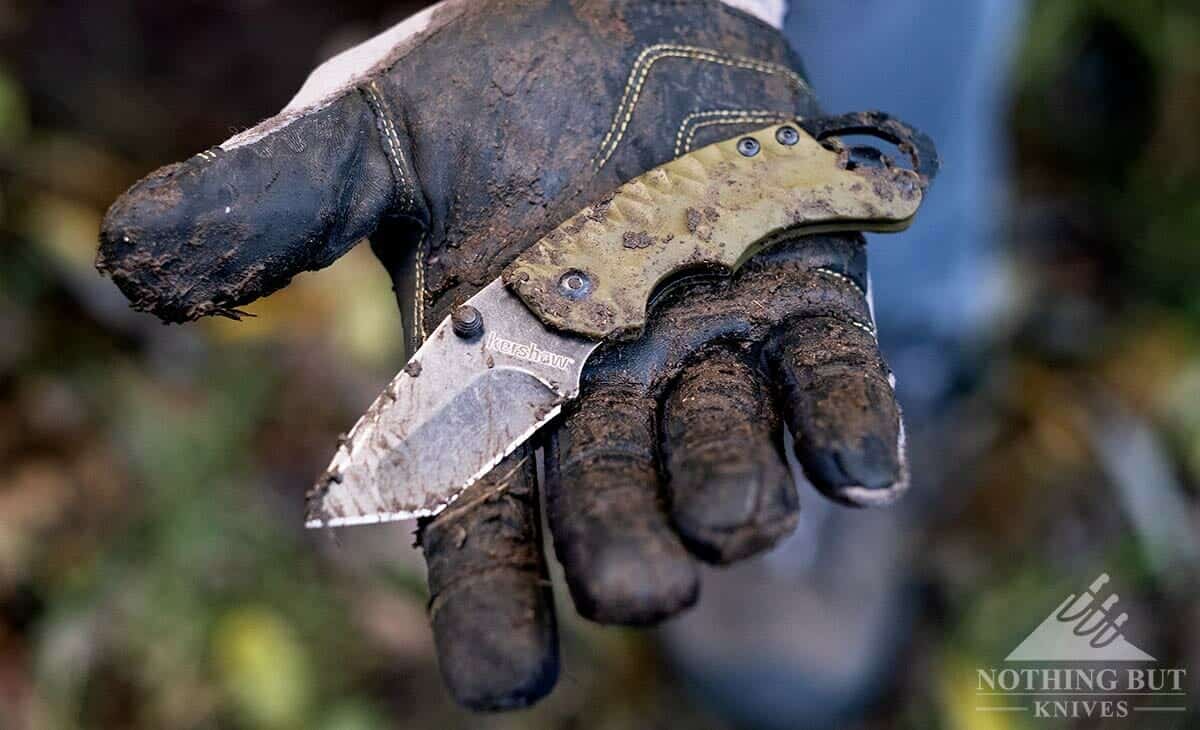 A pocket knife in a gloved hand all muddy from cutting irrigation pipe in the ground. 