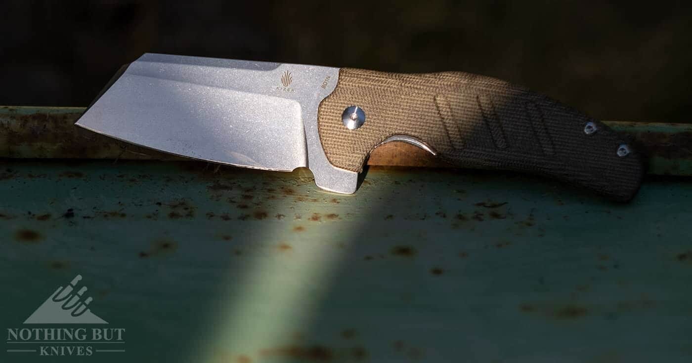 Best Hard Use Pocket Knives Under $50 And $100 - Image 44 The Kizer Sheepdog sitting on a rusty of piece of metal.