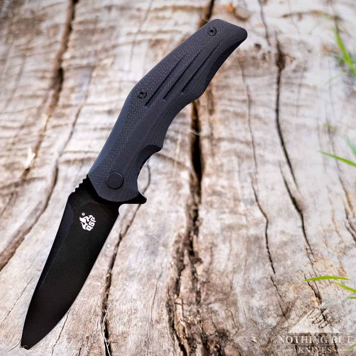 The all black version of the QSP Pangolin hard use knife with the blade sticking into a tree stump.