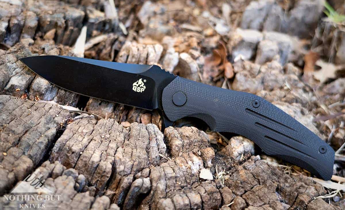 The QSP Pangolin pocket knife in the open position on a tree stump outdoors.