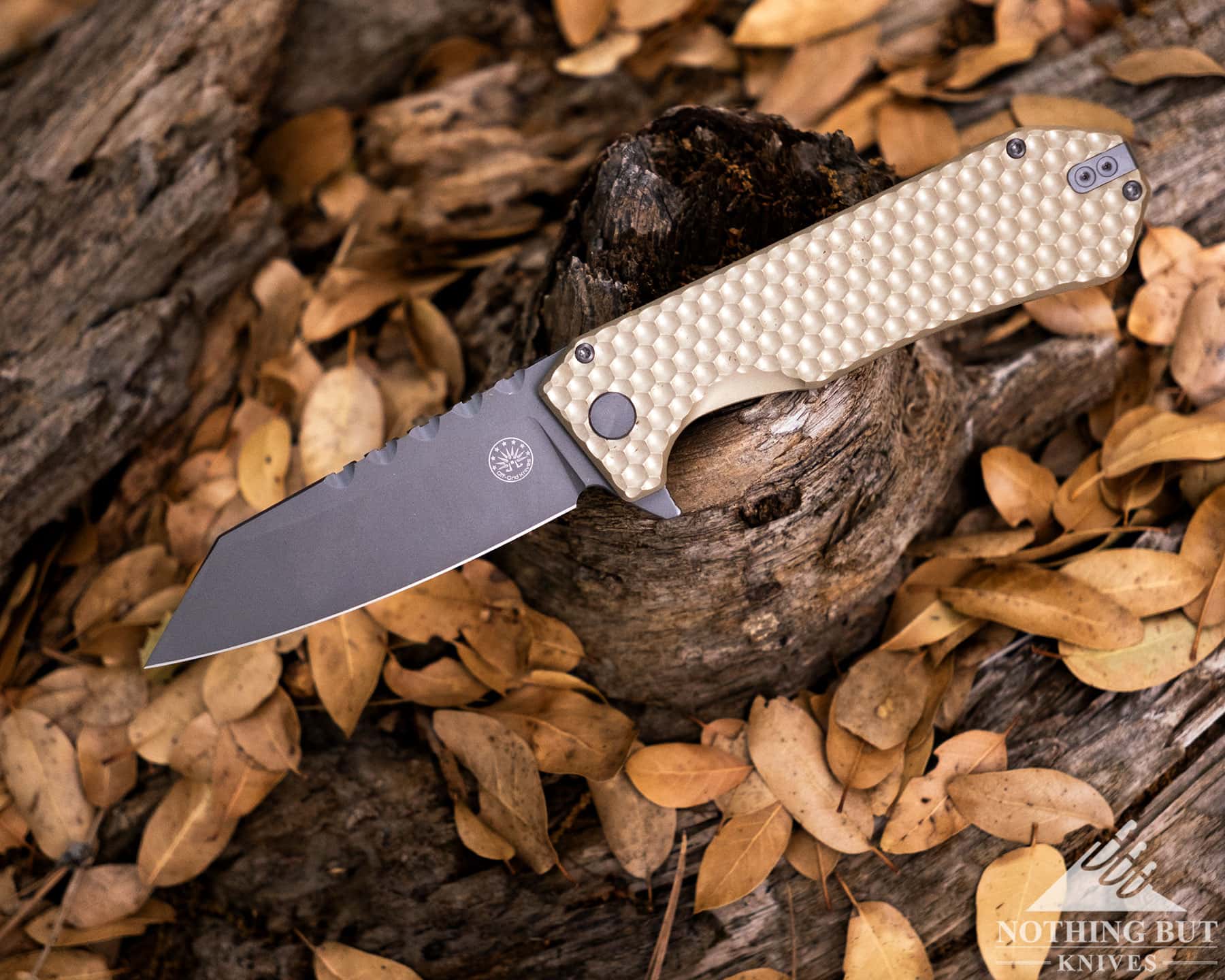 The Best Tactical Knives From Our Favorite Brands - Image 48 An overhead view of the Coyote gold version of the Off-Grid Black Mamba shown here with its blade in the open position above Oak leaf covered ground in a forest. ground i