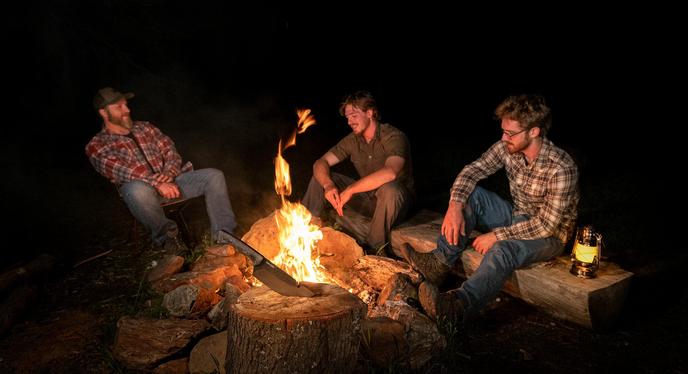 The crew of Nothing But Knives sitting around a campfire after a day of testing knives in the wilderness.