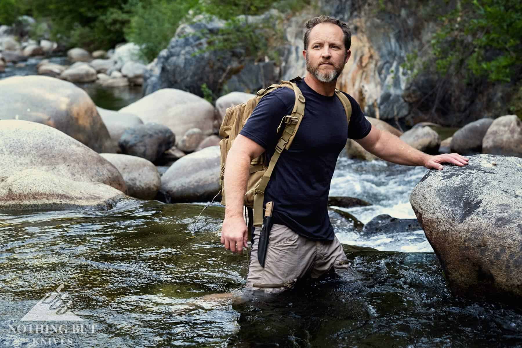 A man crossing a creek while wearing the Buck Compadre camp knife as part on an in-depth review. 