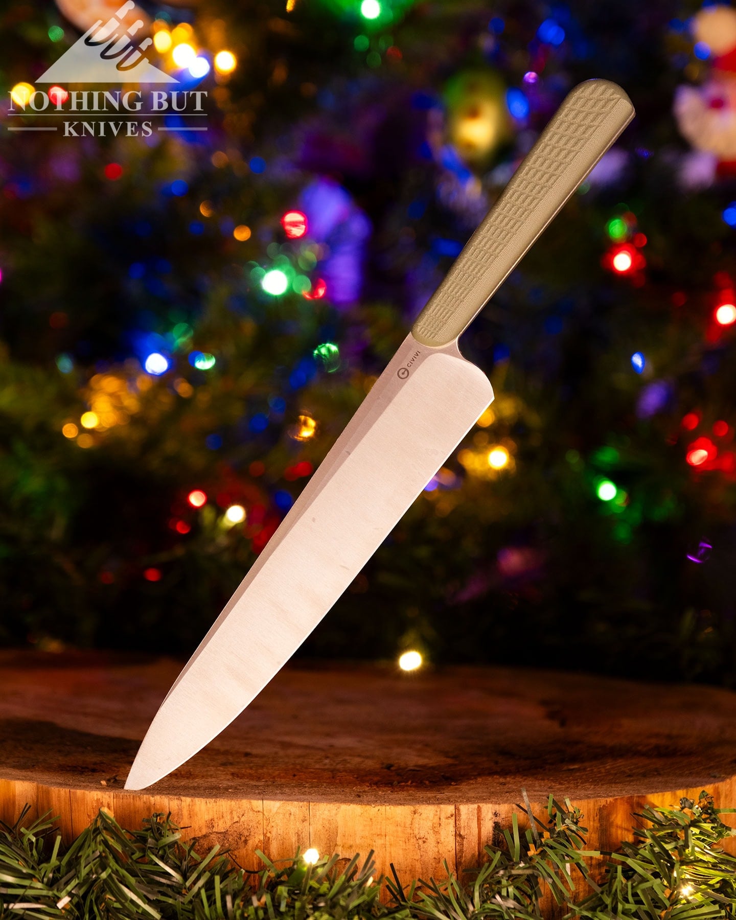 A shallow depth of field image of the Civivi Cibus chef knife with its blade tip sticking out of a cedar round in front of a decorated Christmas tree.