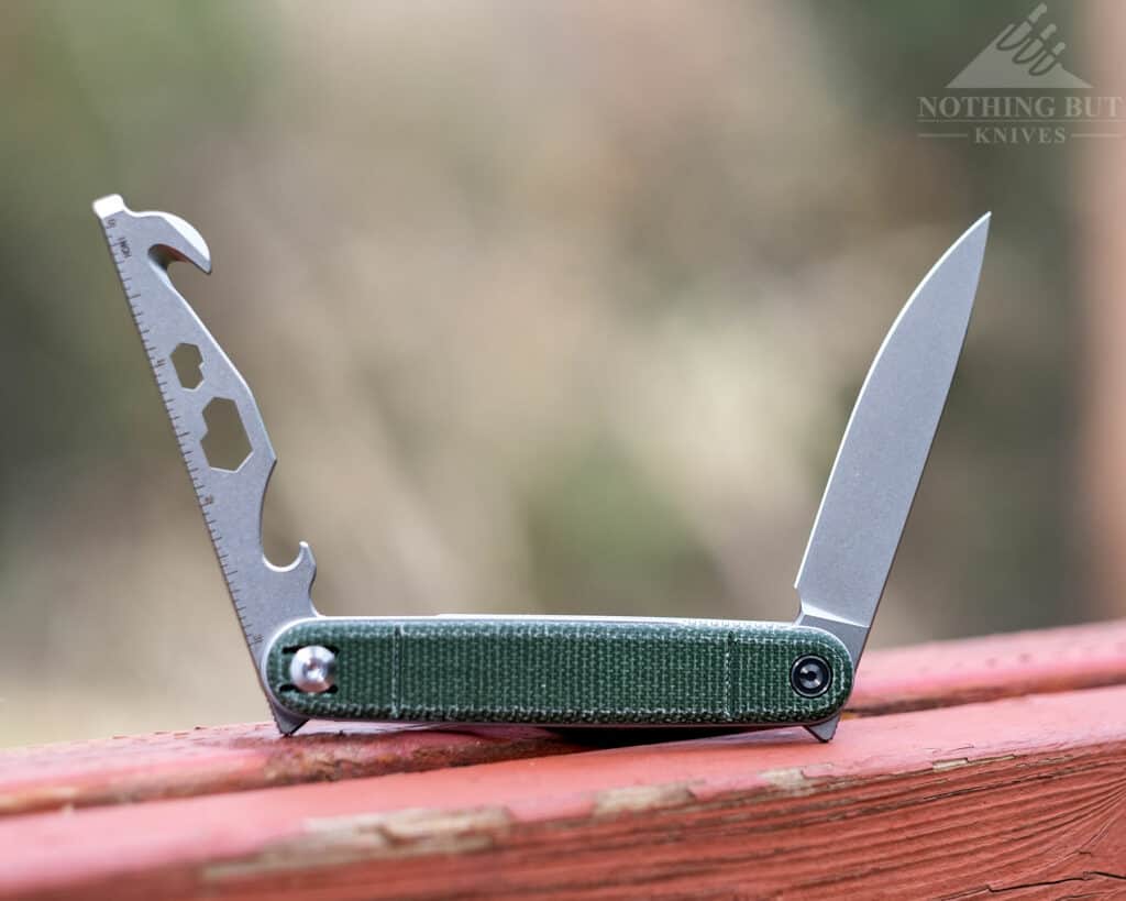 The Civivi Crit multi-tool pocket knife outdoors on a fence with both the blade and tool bar in the open position.