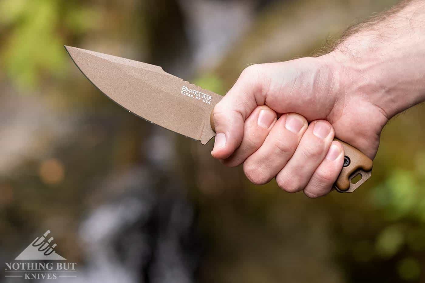 A man's hand holding the Ka-Bar BK18 Harpoon Fixed blade knife outdoors next to a mountain creek.