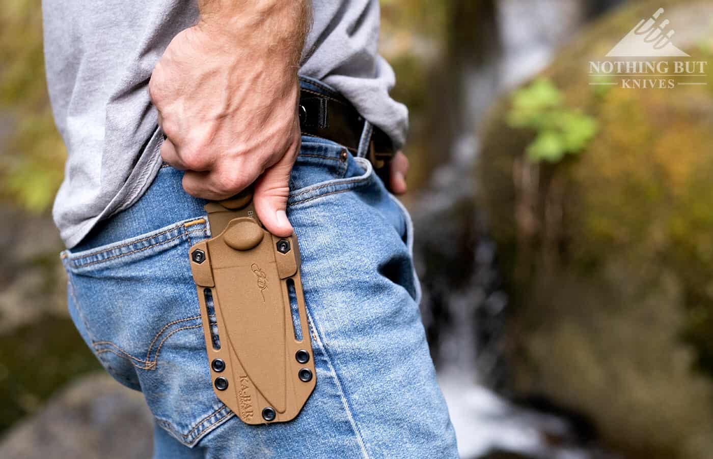 A man drawing the Ka-Bar Becker BK18 Harpoon survival knife from it's sheath while hiking outdoors.