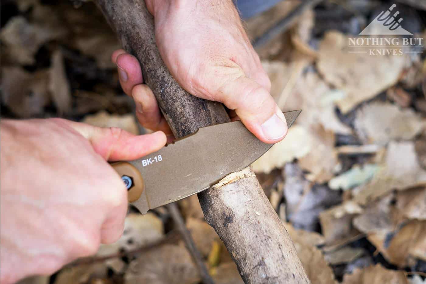 A man's hands carving a notch in a branch with the Ka-Bar Becker BK18 Harpoon survival knife. 