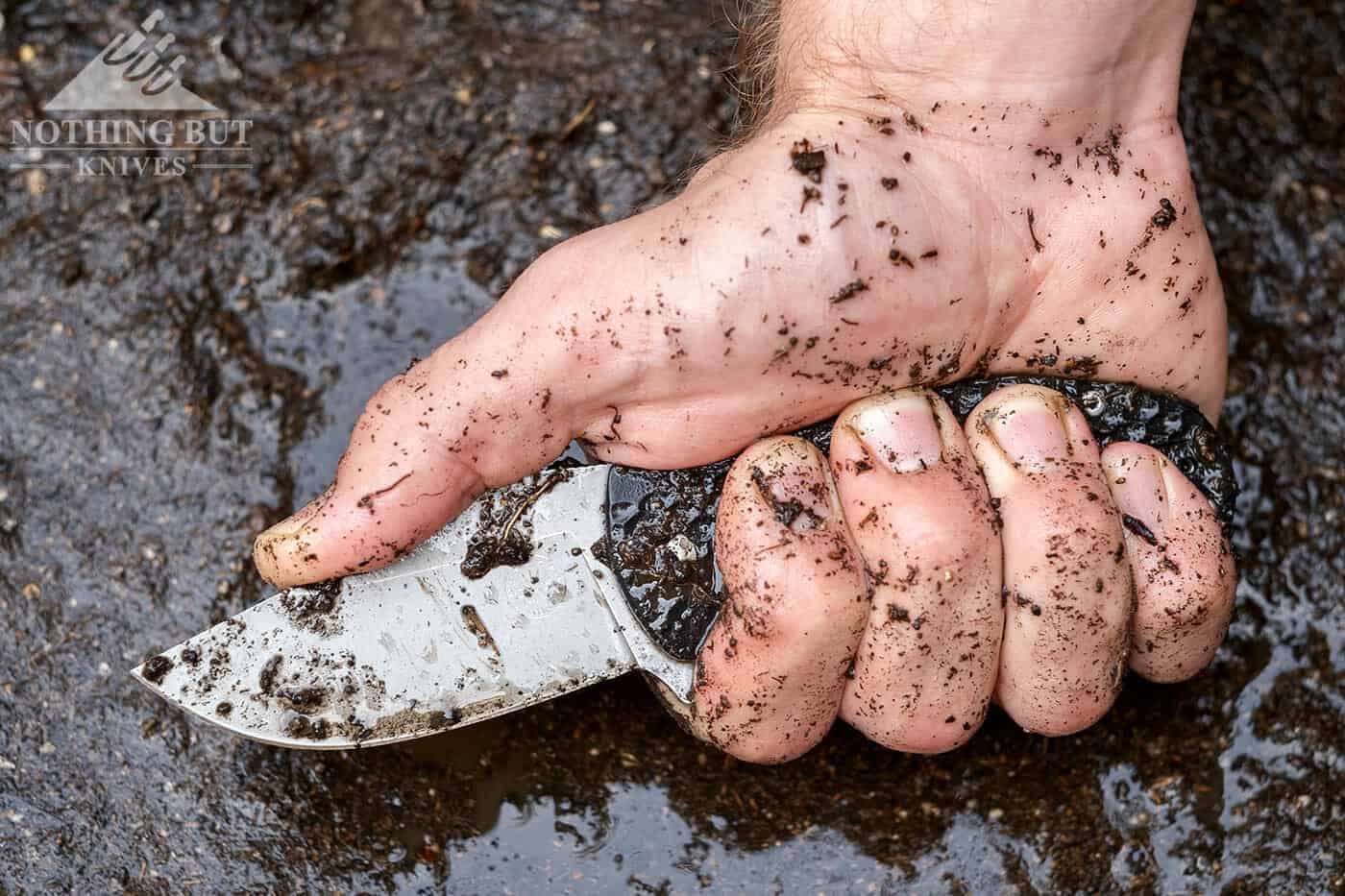 Dirty pocketknife held by a muddy hand.