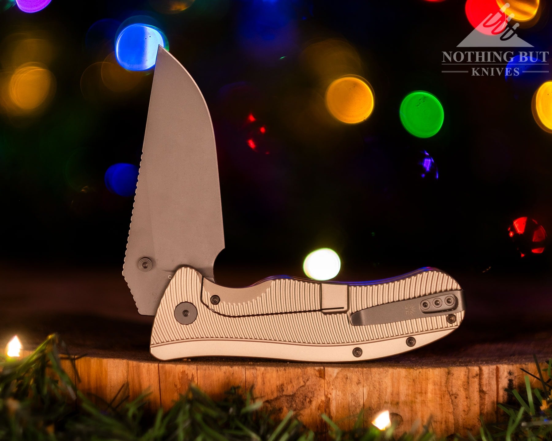 A right profile view of the Off-Grid Rhino Elite folding knife with its blade in the half open position in front of blurry holiday lights.