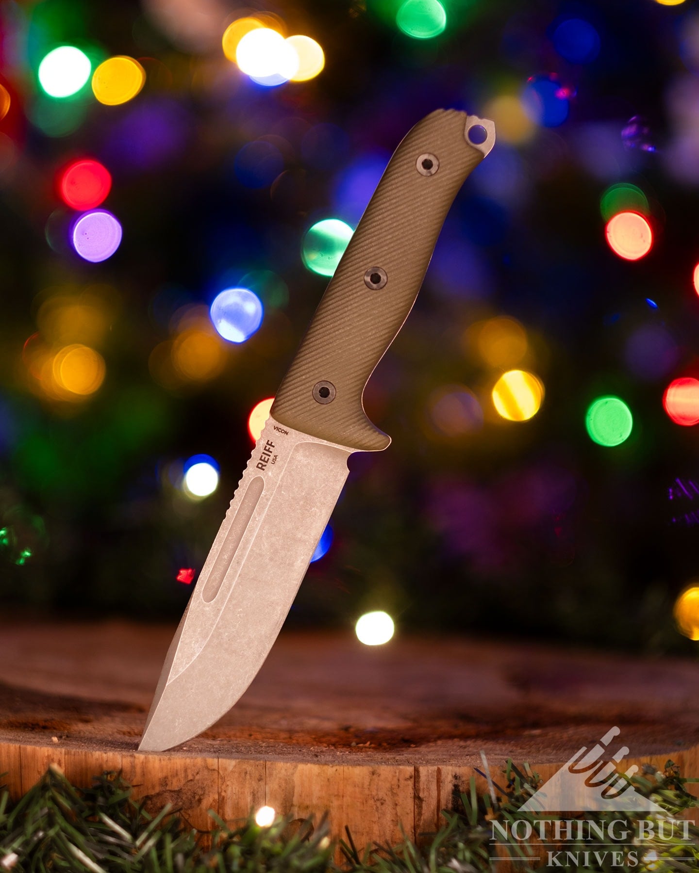 A left profile view of the Reiff Vicon survival knife on a piece of wood in front of a Christmas tree. 