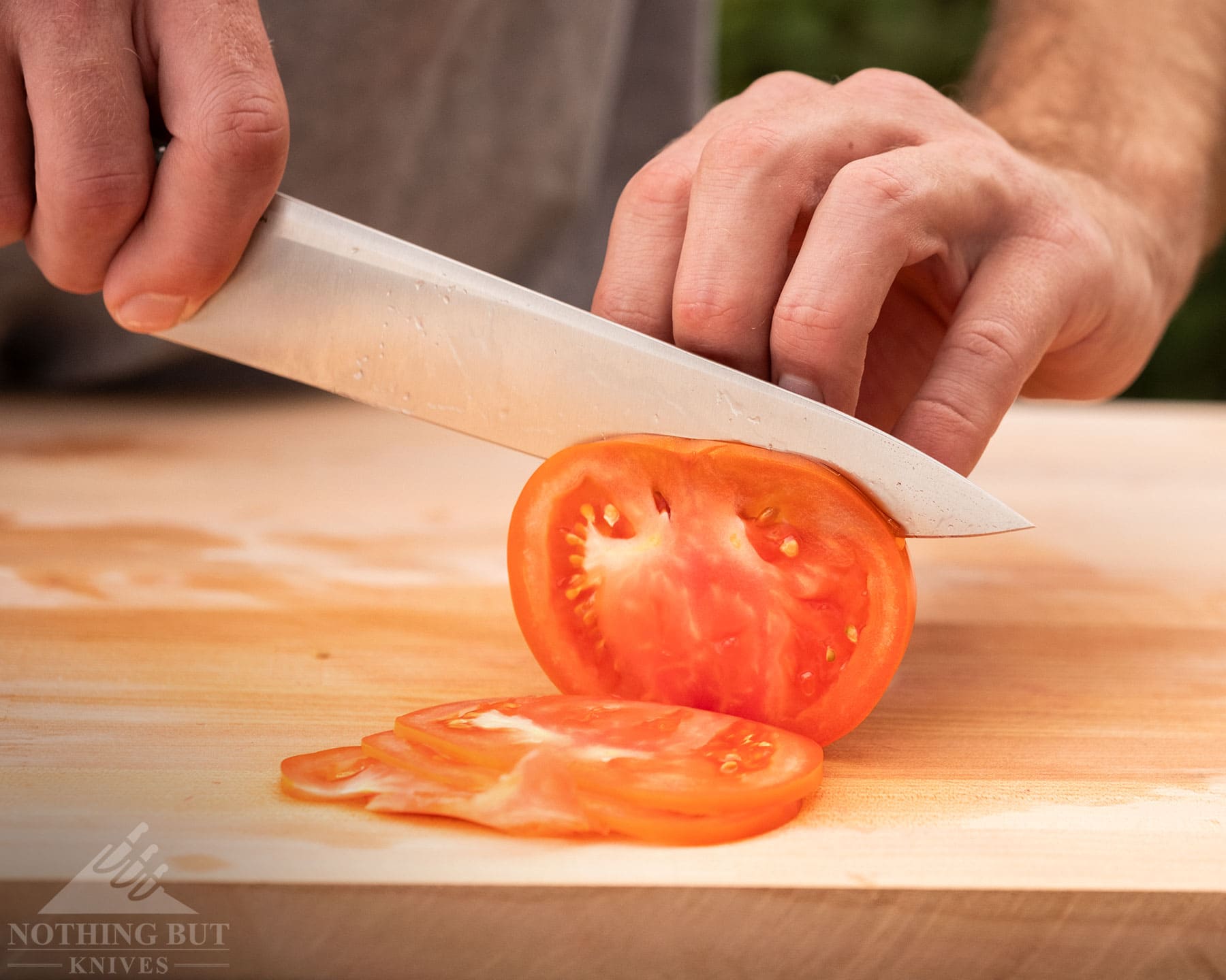 A close-up of the Civivi Cibus chef knife being used to slice a tomato on a Bamboo wood cutting board. 