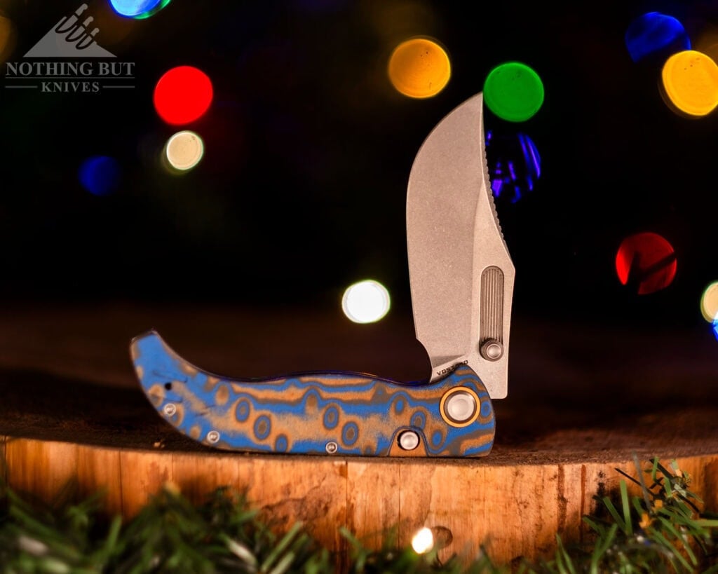 The Vosteed Naga EDC pocket knife with ocean Micarta handle scales and an S35VN steel blade shown here with its blade in the have open position in front of a decorated Christmas tree. 