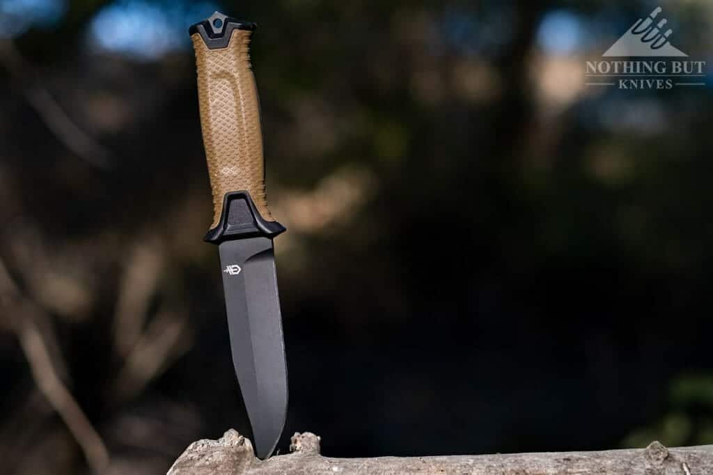 The Gerber StrongArm tactical survival knife stabbed into a log in the woods.