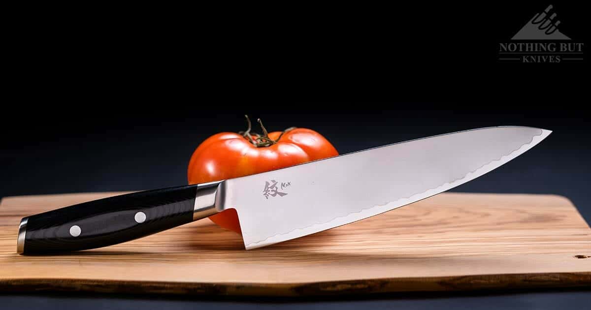A Yaxell Mon chef knife on a cutting board with a tomato