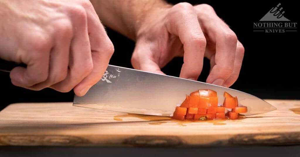 The Yaxell Mon chef knife chopping a tomato on a wood cutting board.