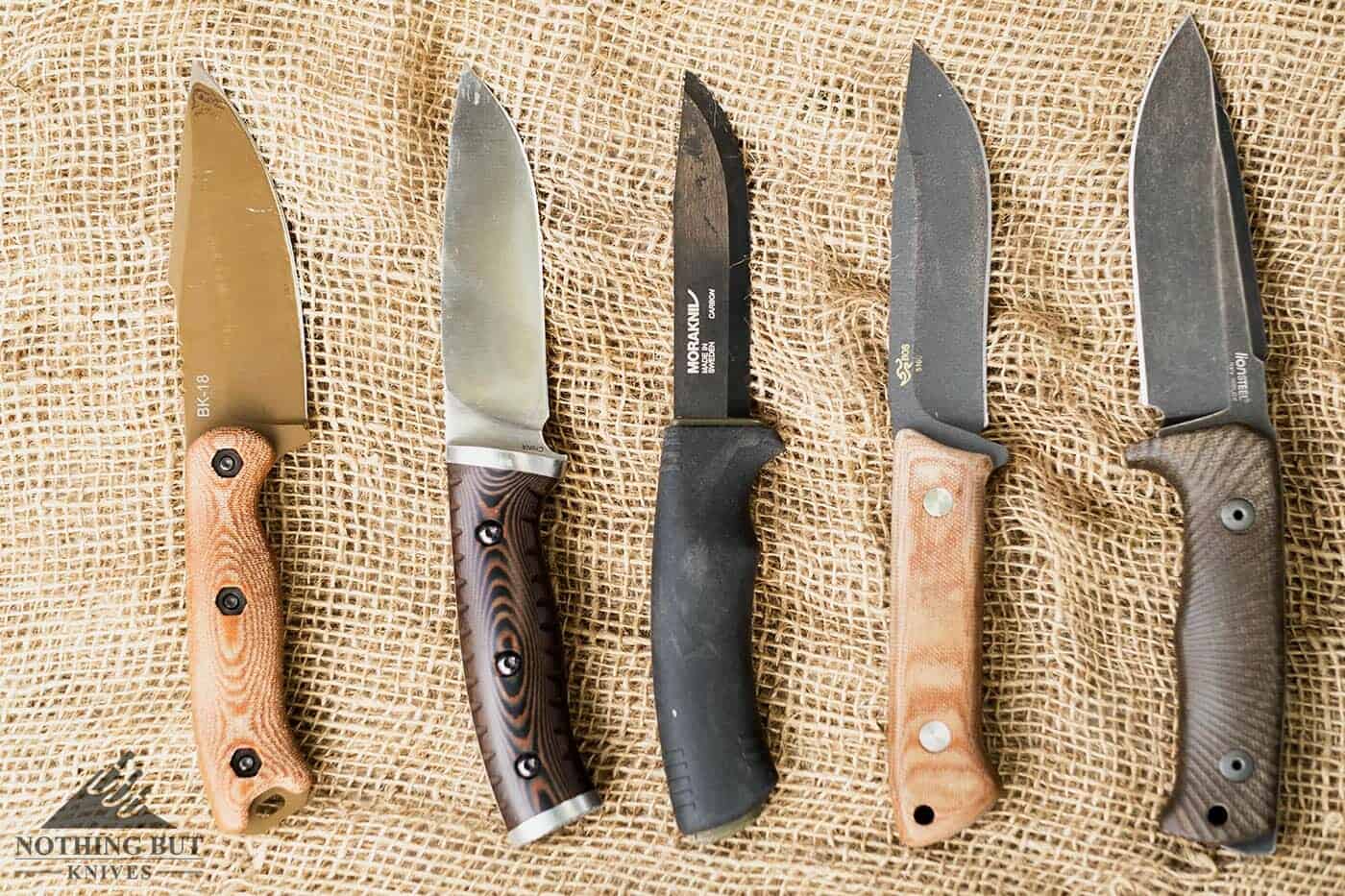 Five different survival bushcraft knives on a burlap background.