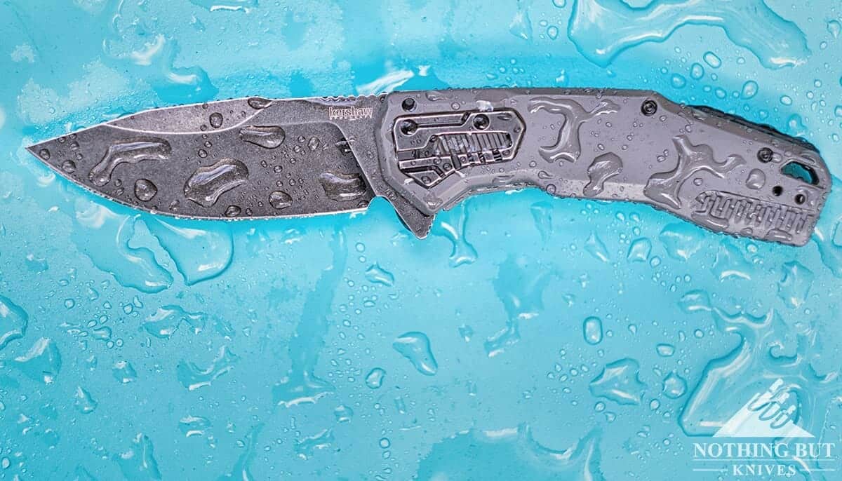 The Best D2 Steel Knives And What Makes Them Great 6 The Kershaw Cannonball pocket knife covered in water drops with the blade open on a blue background.