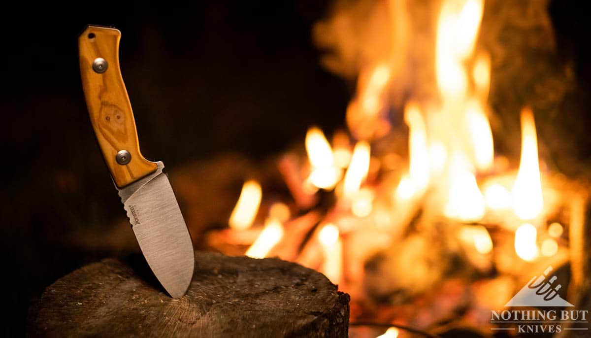 The LionSteel M2 Hunter fixed blade knife sticking out of a tree stump next to a camp fire. 
