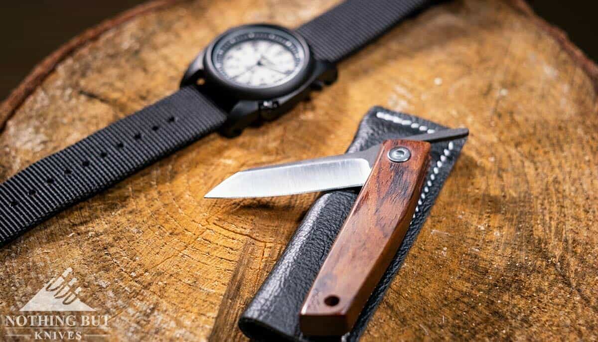 The Ohta Knives FK5 partially open on a tree stump with a field watch. 
