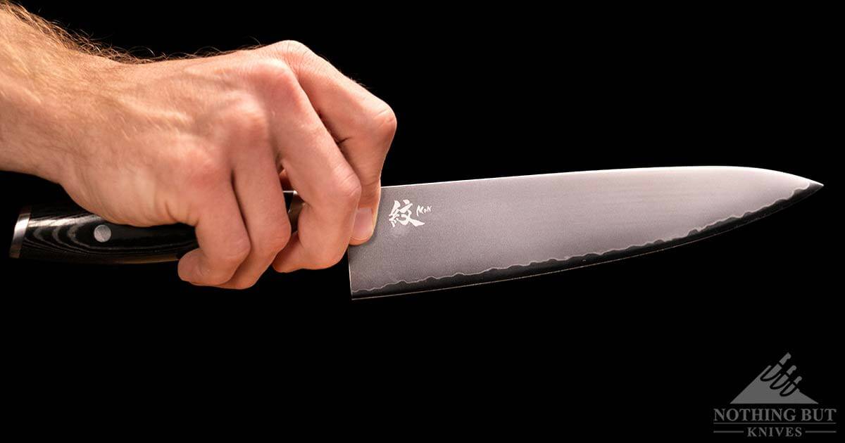 A close-up of a man's hand holding a Yaxell Mon chef knife in a pinch grip.
