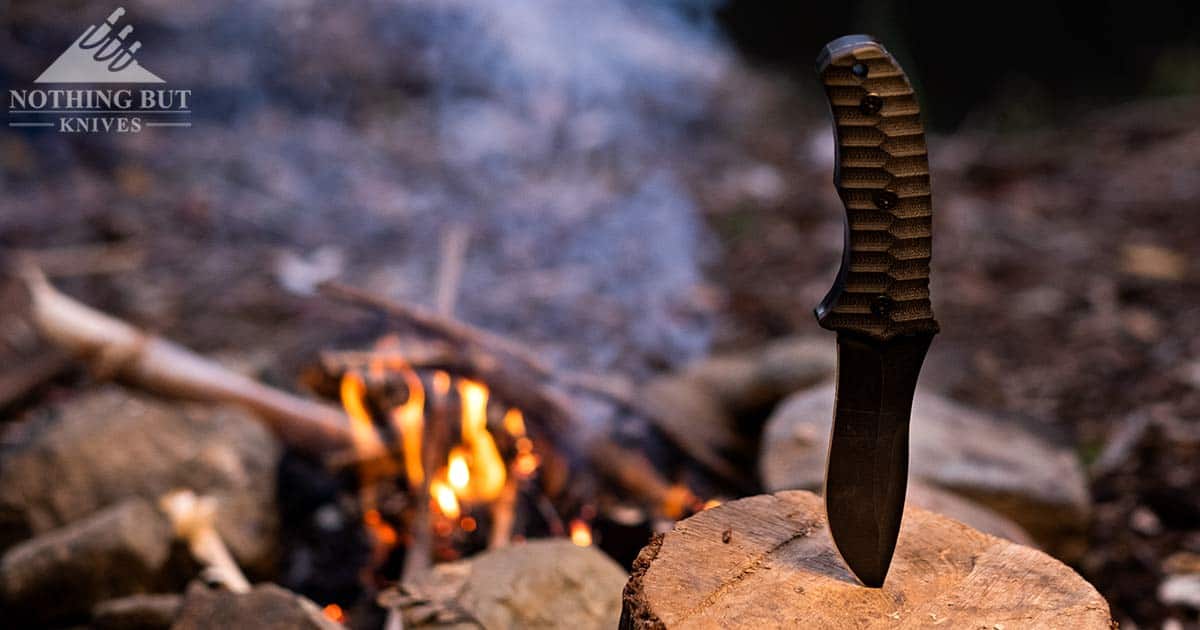 The Backcountry fixed blade knife sticking out of a stump next to a campfire.